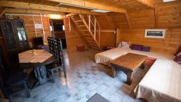 A cozy attic room with a wooden floor, a bed, a desk with a chair, and a staircase.