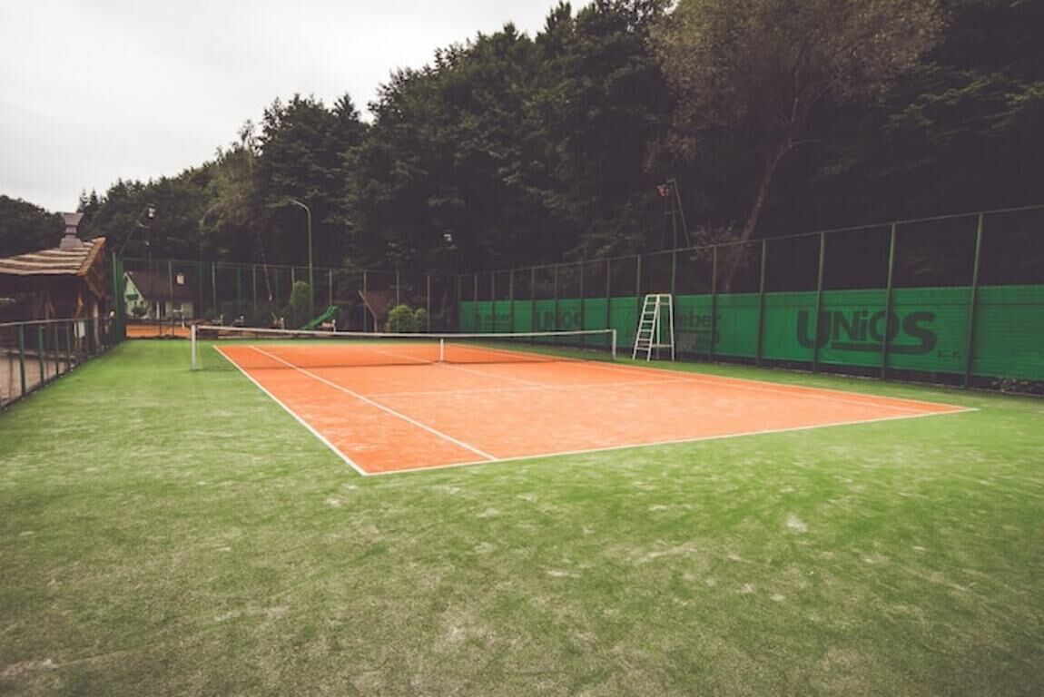 A tennis court with a green fence and a UNIOS banner.