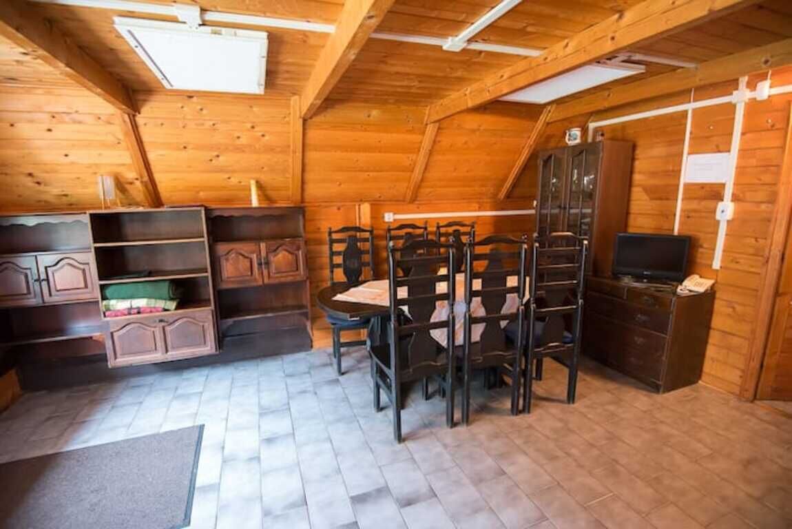 A wooden interior with a dining table and chairs, built-in shelving, and a television.