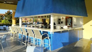 A blue outdoor bar area with white bar stools and a counter.