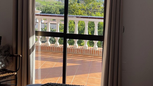 Une pièce dotée d’une grande porte-fenêtre coulissante donnant sur un balcon carrelé, agrémenté d’une balustrade blanche.