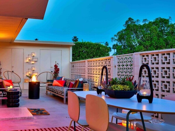 An outdoor patio area with a dining table, chairs, a sofa, and a decorative wall.