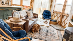 A cozy, open-plan living space with a wooden ceiling, a sofa, a chair, a rug, and a dog. - Private Romantic Luxury Yurt- Sunset deck with Mt Views-Hot Tub-AC-WiFi-Fire Pit (Woodstock)