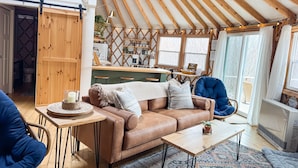 A cozy interior with a sofa, coffee table, and a dining area. - Private Romantic Luxury Yurt- Sunset deck with Mt Views-Hot Tub-AC-WiFi-Fire Pit (Woodstock)
