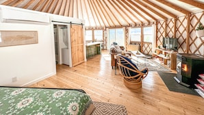 A yurt interior with a wooden ceiling, a central seating area, a fireplace, and a kitchen area. - Private Romantic Luxury Yurt- Sunset deck with Mt Views-Hot Tub-AC-WiFi-Fire Pit (Woodstock)
