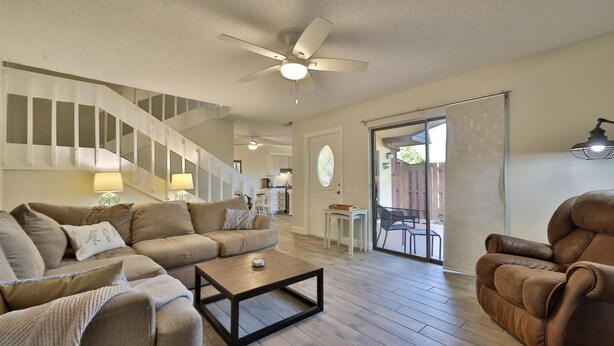 A spacious living area with a sofa, armchair, and coffee table, a staircase, and a view through a glass door.