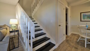 A staircase with white railings leading to a second floor, a dining area with a table and chairs, and a lamp on a side table.