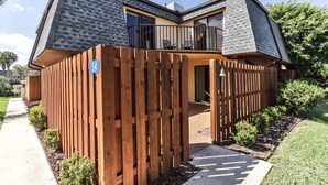 A modern two-story house with a balcony, a wooden fence, and a clear sky.