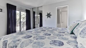 A bedroom with a large bed, a view through the window, and a door leading to another room.