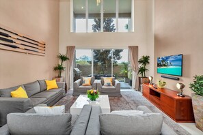 A spacious living area with a grey sofa set, a coffee table with a vase, and a wooden entertainment unit.
