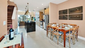 Une cuisine moderne équipée d’appareils électroménagers en acier inoxydable, un coin repas avec une table et des chaises en bois, et un escalier menant à l’étage supérieur.