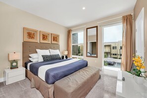 A hotel room with a large bed, a bedside table with a lamp, a window with curtains, and a view of the outside.