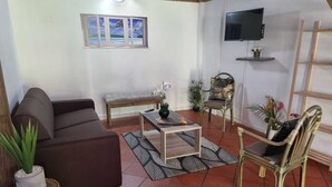 Uma sala de estar com um sofá, uma mesa de centro, uma poltrona e uma TV fixada na parede.