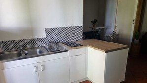 Uma cozinha compacta com armários brancos, bancada de madeira e painel atrás do fogão em azulejos.