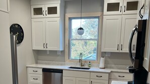 Une cuisine moderne avec des meubles blancs, un lave-vaisselle en acier inoxydable, une cuisinière noire et une fenêtre donnant sur un paysage verdoyant.