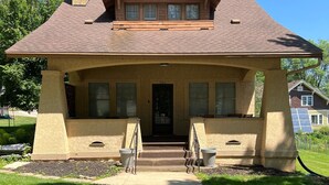 Une maison à deux étages, dotée d’une cheminée imposante, d’un porche à l’avant avec des marches et du numéro « 706 » sur la porte.