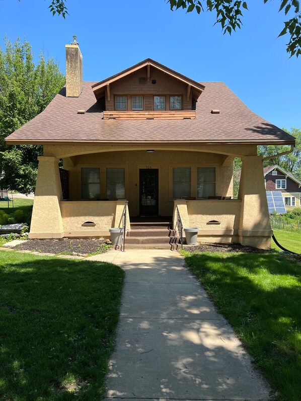 Une maison à deux étages, dotée d’une cheminée imposante, d’un porche à l’avant avec des marches et du numéro « 706 » sur la porte.