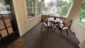 Une terrasse couverte avec une table et des chaises, de grandes fenêtres et une vue sur une maison.