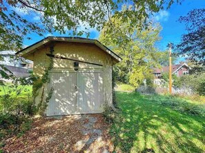 Situated in a residential area, this small structure offers a setting amidst a well-maintained lawn and shaded trees.