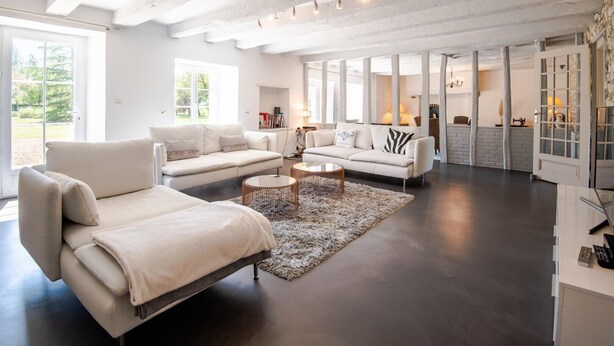 A spacious living room with a large sofa, a smaller sofa, and a coffee table. There are large windows providing natural light and a view of greenery outside. - Longère classée 4 étoiles - piscine  – Ambillou (Ambillou)