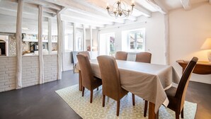 A dining area with a table set for four, surrounded by chairs. A chandelier hangs from the ceiling, and the room has exposed brick walls and a stone fireplace. - Longère classée 4 étoiles - piscine  – Ambillou (Ambillou)