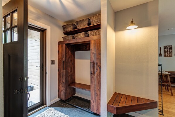 A hallway with a wooden door, a bench, and baskets on shelves.