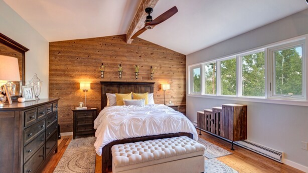 A bedroom with a wooden ceiling, a large bed, bedside lamps, a bench, and a view of trees through a window. - Mountain Modern Condo on EagleVail Golf Course near Vail and Beaver Creek (Avon)