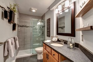 A modern bathroom with a glass shower enclosure, a toilet, a sink with a vanity, and a large mirror.