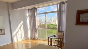 A hotel room with a large bed, a small table, and a view of the city through large windows. - Luminosidade, in front of Parque da Luz / 5 minutes from the Metro. (São Paulo)