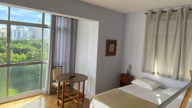 A bedroom with a large window, a bed, a small table, and a chair. - Luminosidade, in front of Parque da Luz / 5 minutes from the Metro. (São Paulo)