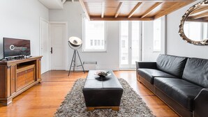 A modern living room with a wooden ceiling, a black leather sofa, a wooden TV stand, and a floor lamp.