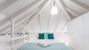 A bedroom with a sloped ceiling, a bed with teal bedding, and white walls.