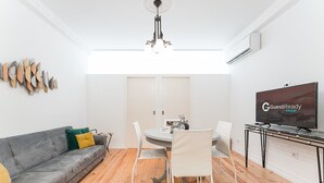 A modern living room with a grey sofa, white chairs, a round dining table, and a flat-screen TV. - GuestReady Economy - Gold Leaf GF (Porto)