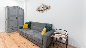 A grey sofa with yellow and green cushions, a grey cabinet, and a wall-mounted decorative piece. - GuestReady Economy - Gold Leaf GF (Porto)