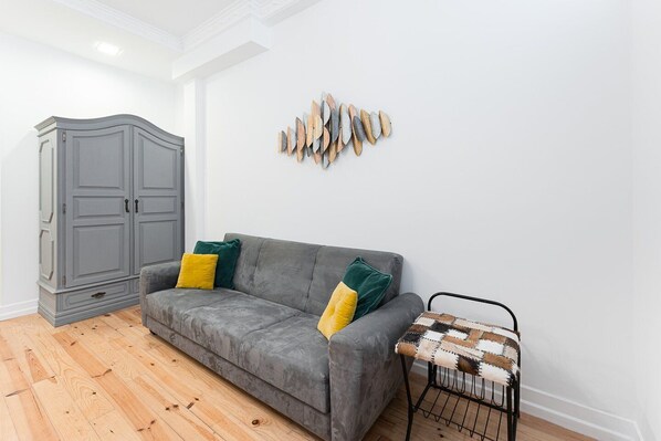 Un canapé gris agrémenté de coussins jaunes et verts, un meuble gris et un élément décoratif fixé au mur.