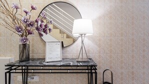 A bathroom vanity with a marble countertop, a round mirror, a vase with purple flowers, a framed menu, and a modern floor lamp. - GuestReady Economy - Gold Leaf GF (Porto)
