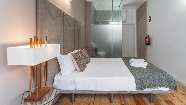 Ein modernes Hotelzimmer mit einem großen Bett, einer Nachttischlampe, einer Duschkabine aus Glas und einem Feuerlöscher.