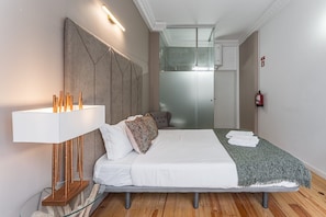 Una habitación de hotel moderna con una cama grande, una lámpara de noche, un box de ducha de vidrio y un extintor.