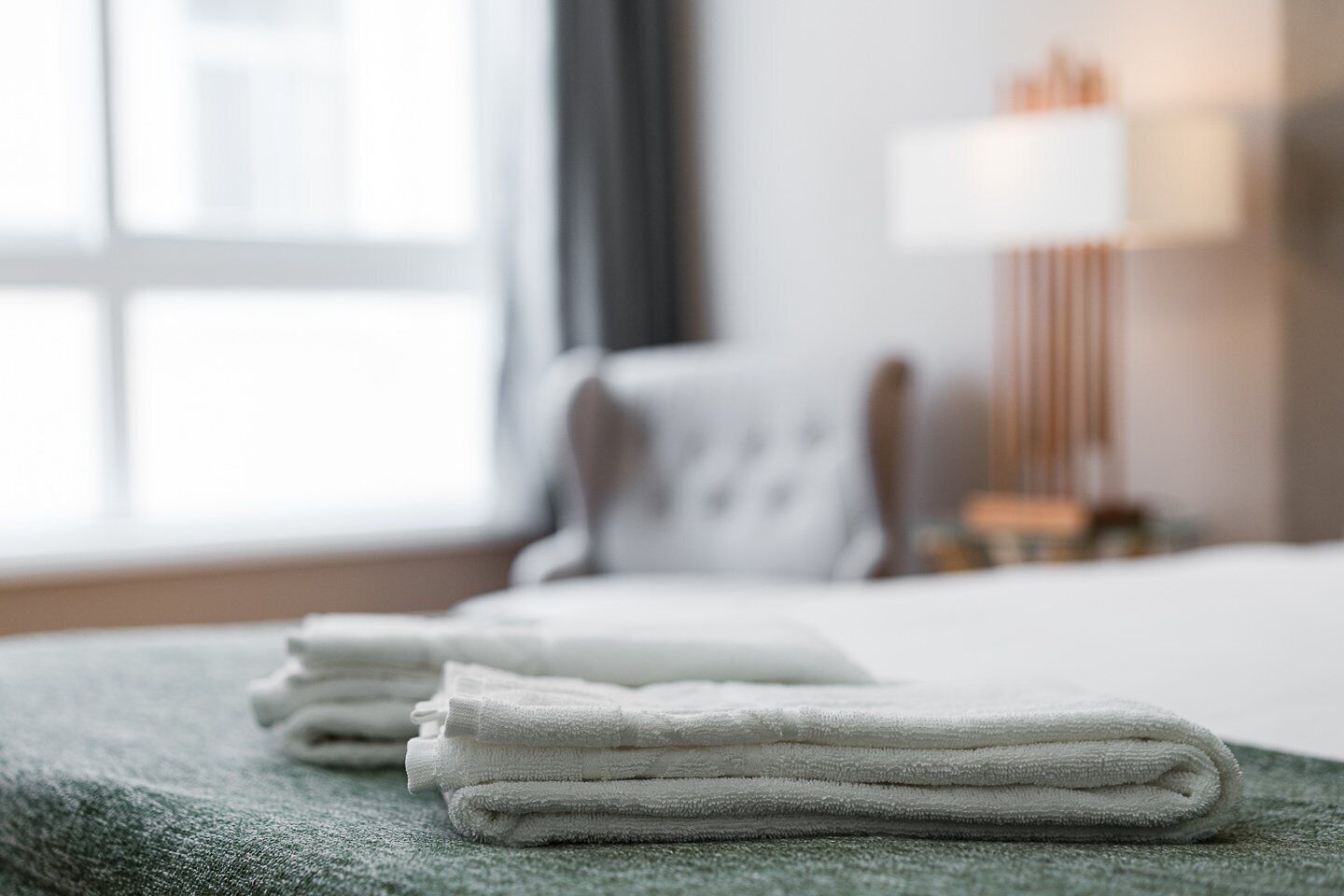 A neatly folded stack of white towels on a green textured surface in a hotel room.