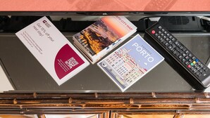 Habitació d'hotel amb un armari de fusta, un comandament a distància, un mapa de Porto i una targeta promocional.