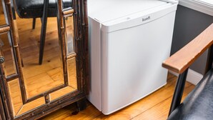 Un aparell blanc i compacte, possiblement un frigorífic, en una habitació amb sòls de fusta i una cadira.