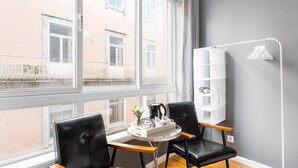 Habitació moderna amb dues cadires de pell negra, una taula rodona petita amb una cafetera i un moble d'estanteries blanc davant d'una paret gris.