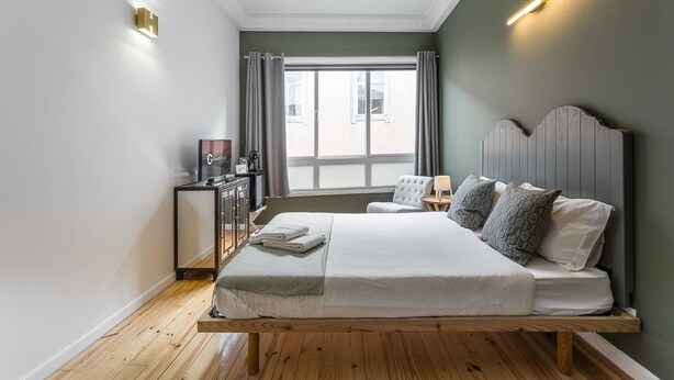Une chambre d’hôtel moderne avec un lit en bois, une table de chevet, une télévision et une vue sur la ville grâce à de grandes fenêtres.