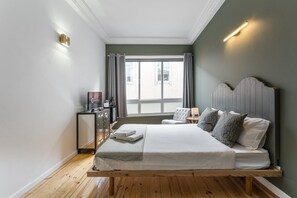 Une chambre d’hôtel moderne avec un lit en bois, une table de chevet, une télévision et une vue sur la ville grâce à de grandes fenêtres.