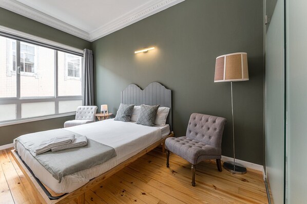 Une chambre avec un grand lit, une table de chevet avec une lampe, une chaise et un lampadaire.