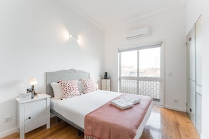 Ein Schlafzimmer mit Bett, Nachttischen, Fenster mit Blick und Klimaanlage.