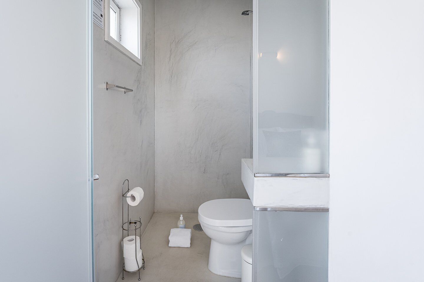A small, modern bathroom with a toilet, a glass shower enclosure, and a marble wall.
