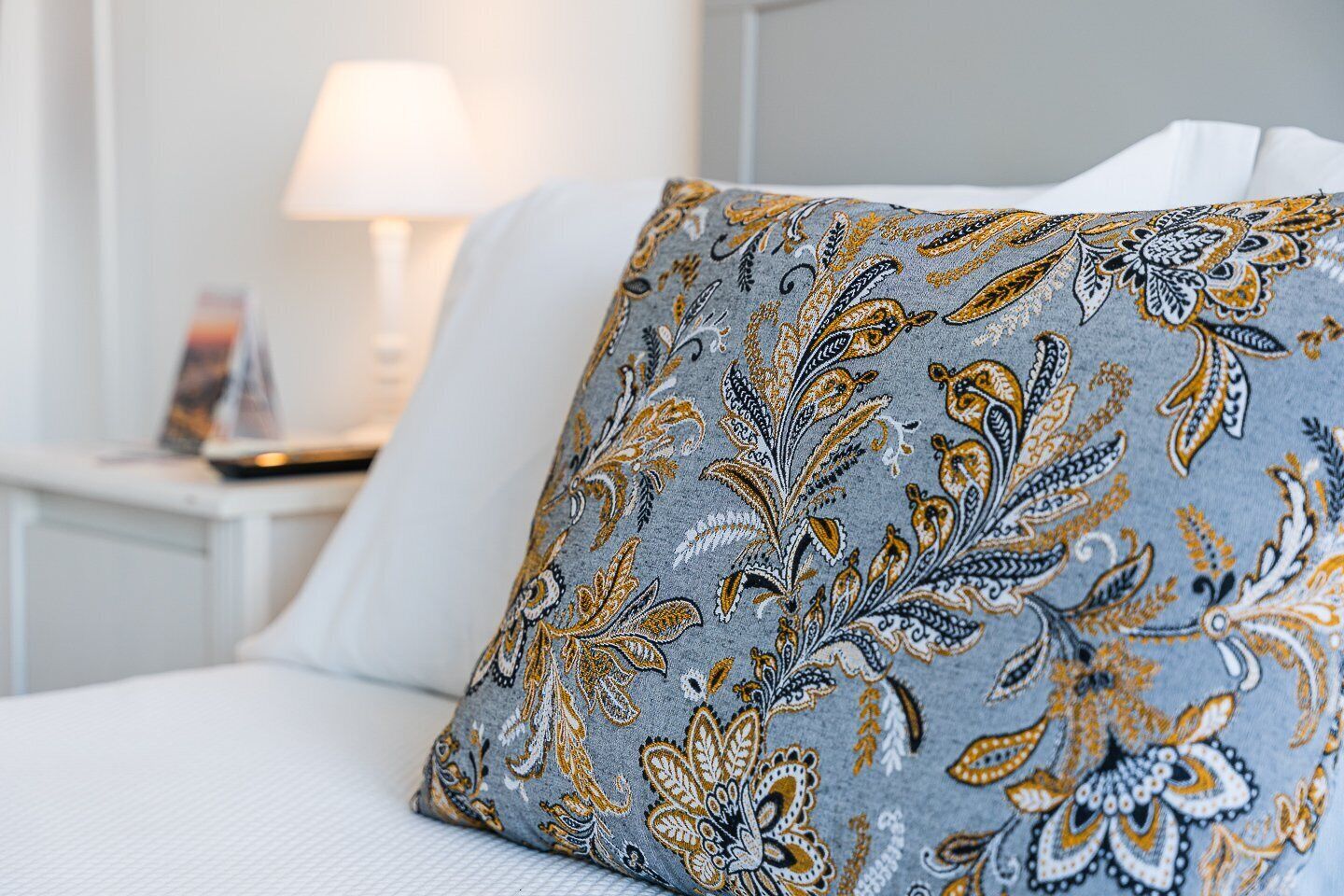 En seng med en grå pude med et paisley-mønster.