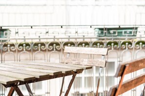 A rustic wooden bench with metal legs, set against a backdrop of white metal railings with green planters.