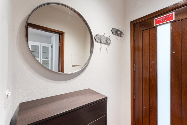 A room with a wooden door, a round mirror on the wall, and a small shelf with decorative items.